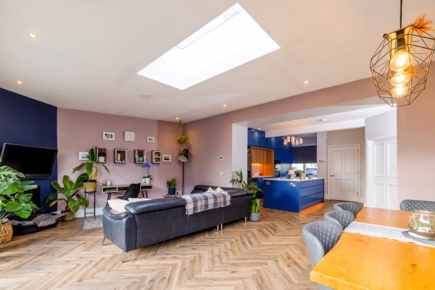 This picture is an open area combining the living room and the kitchen. The room is bright with a navy featured wall and a designed wooden floor.