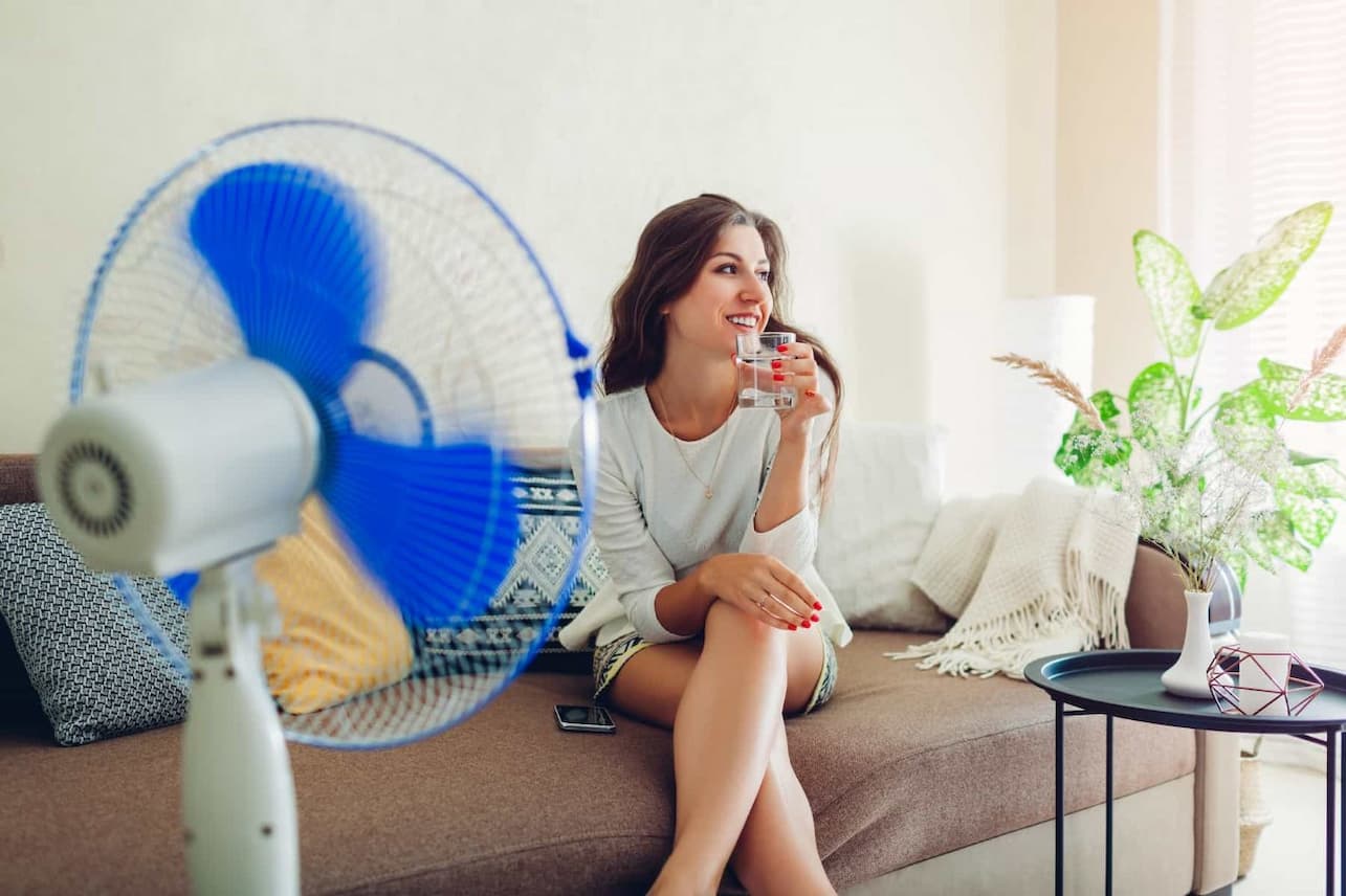 Girl holding glass of water and fan blowing air